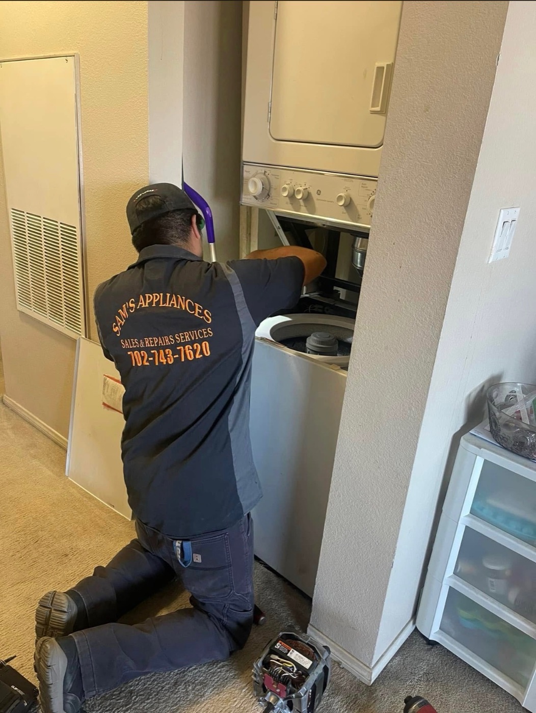 Technician in a Sam's Appliances work shirt repairing a stacked washer and dryer